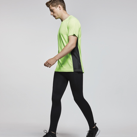 hombre caminando con camiseta verde y mallas negras sobre fondo neutro gris