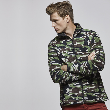 Hombre joven con chaqueta polar de camuflaje mirando de perfil sobre fondo gris claro.