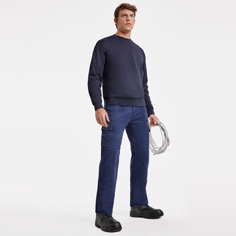 Hombre con sudadera azul marino y pantalones cargo azules sujetando un rollo de cable sobre fondo blanco