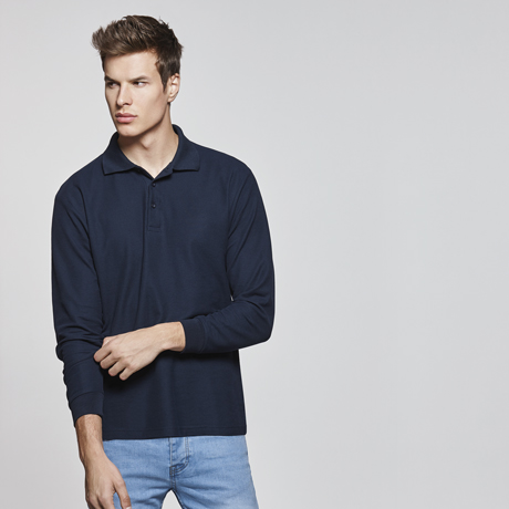 Hombre joven con polo de manga larga azul marino y vaqueros claros sobre fondo neutro