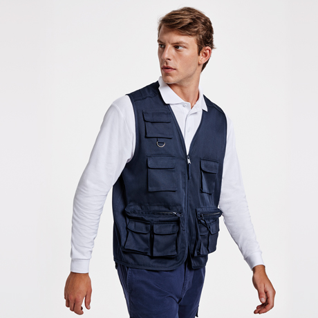 Modelo masculino con chaleco multi­bolsillos azul marino sobre polo blanco en fondo neutro.