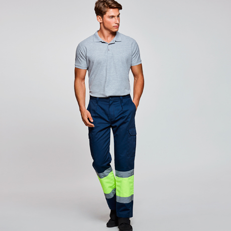 Modelo masculino con polo gris y pantalón de trabajo azul marino con bandas reflectantes amarillas
