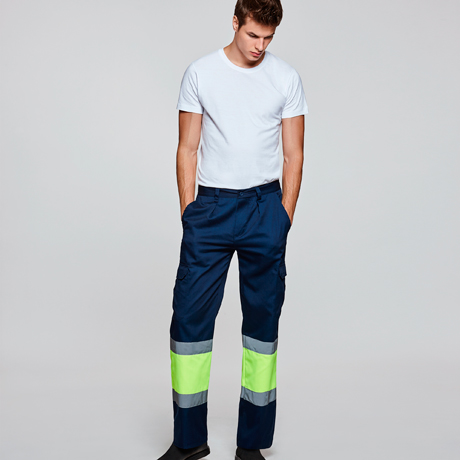 Hombre con camiseta blanca y pantalones de trabajo azul marino con bandas reflectantes verdes y grises.