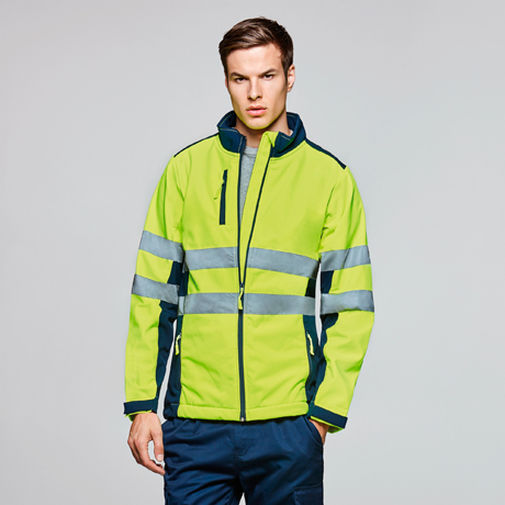 Hombre con chaqueta de alta visibilidad amarilla y bandas reflectantes delante de fondo neutro.