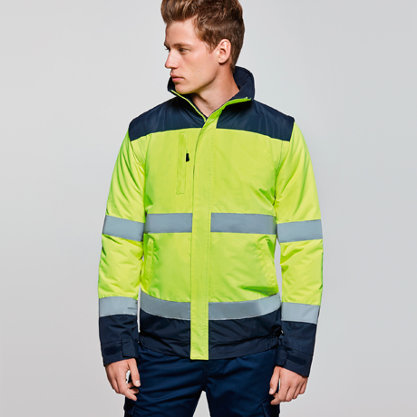 Hombre con chaqueta de alta visibilidad verde y azul marino con bandas reflectantes mirando de perfil sobre fondo neutro
