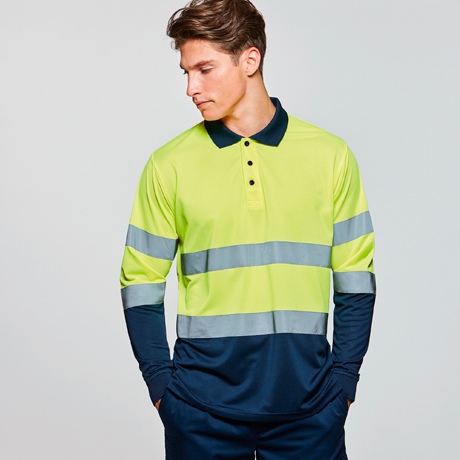 Hombre con polo de alta visibilidad amarillo y franjas reflectantes sobre base azul marino, de pie mirando hacia la izquierda
