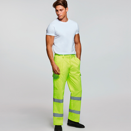 Hombre con camiseta blanca y pantalones de alta visibilidad verdes con bandas reflectantes sobre fondo neutro